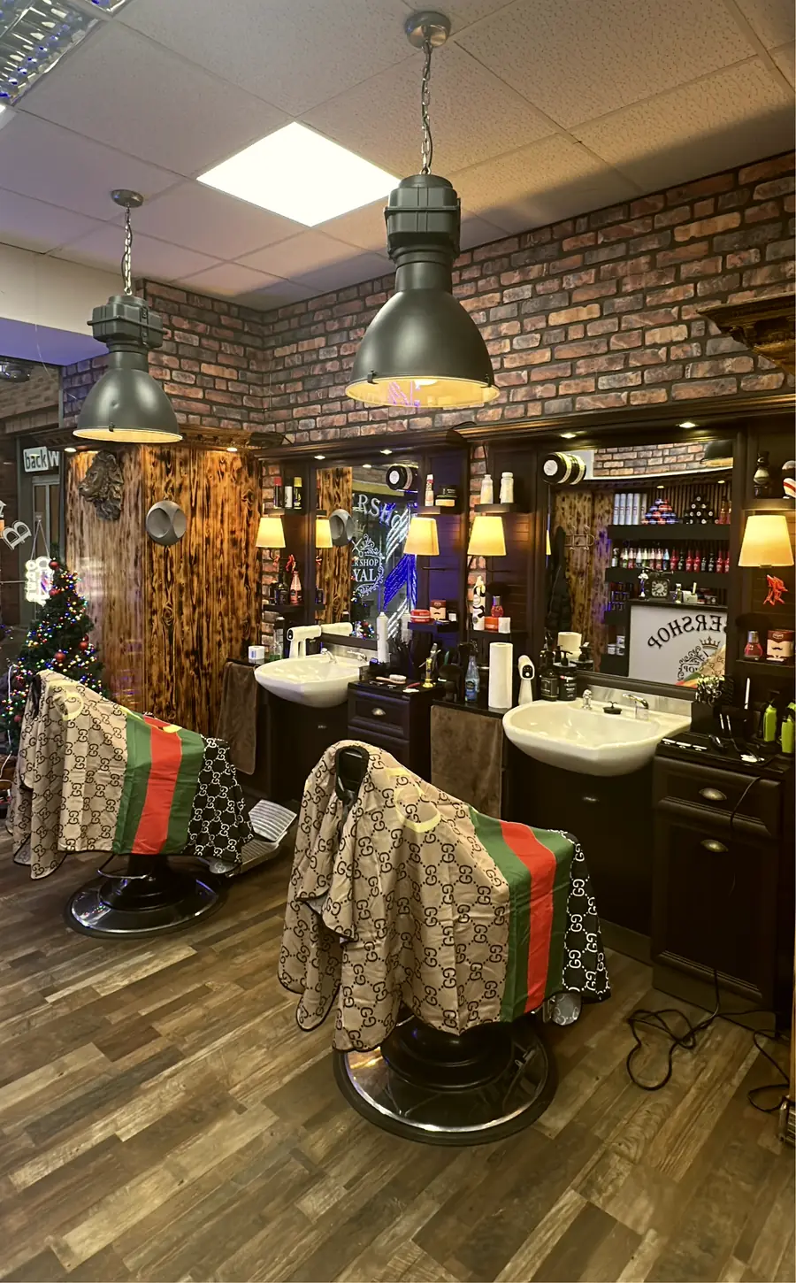 Der Laden innen: zwei Barberstühle, Waschbecken, Wand aus geflammtem Holz und Klinker