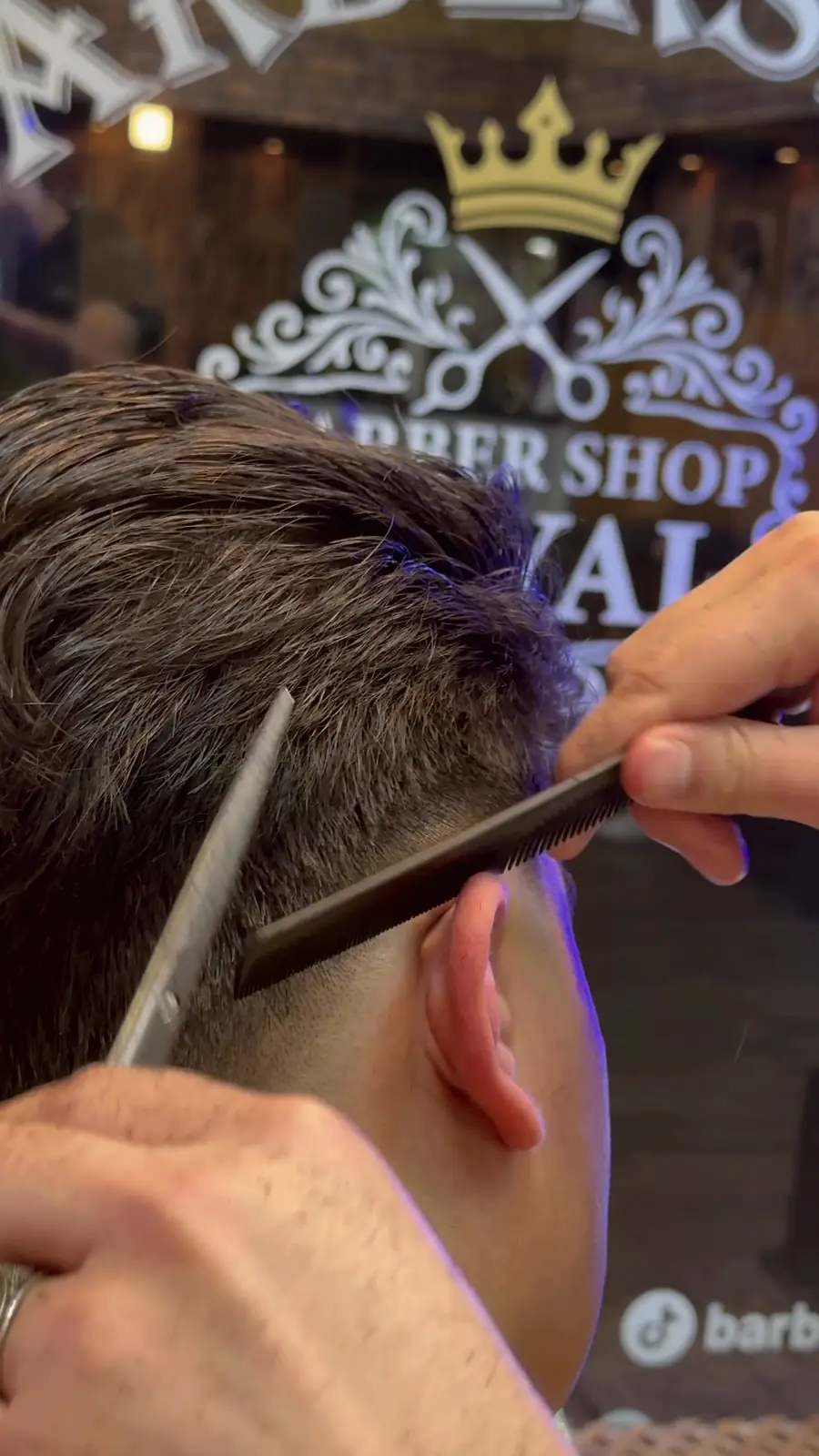 Haarschnitt mit Schere und Kamm vor dem Barbershop-Royal-Logo mit Krone