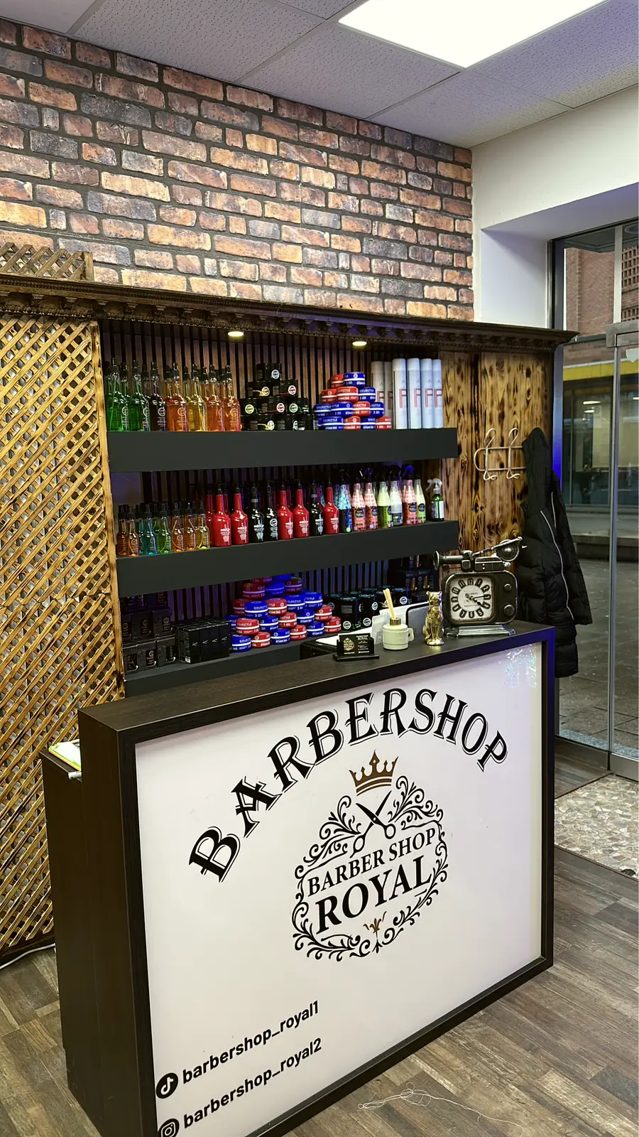 Theke mit Barbershop-Royal-Logo, dahinter Regal mit Stylingprodukten